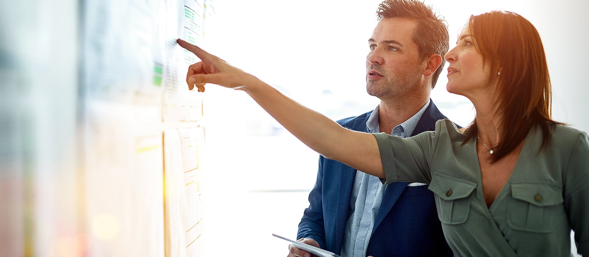 A man and woman look and point at a whiteboard in an office setting